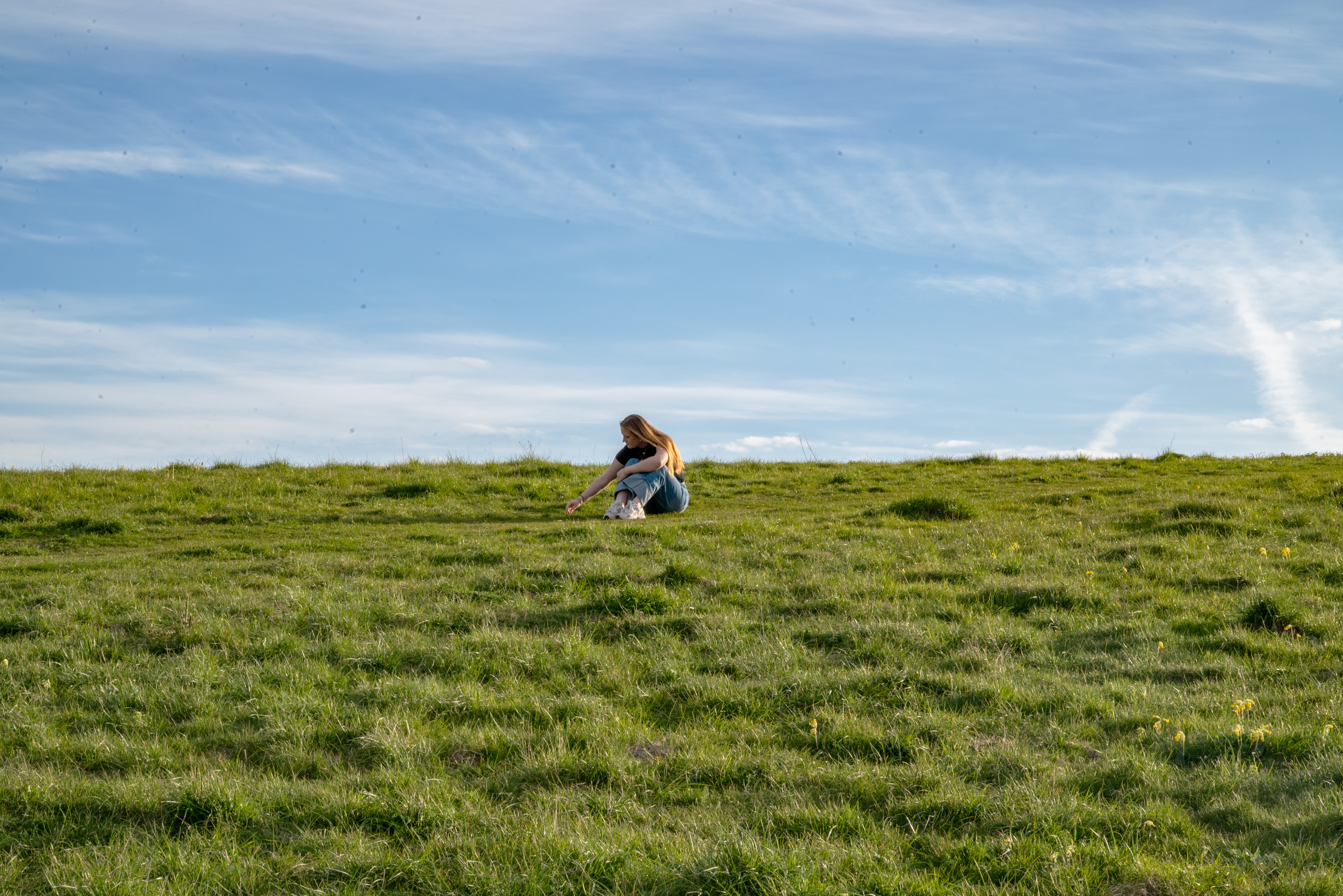 hill: a girl in a black shirt and jeans sitting on top of a hill